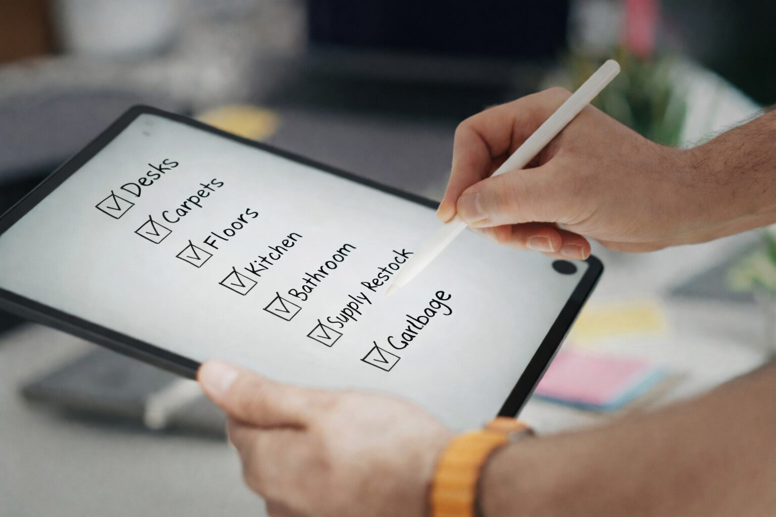 Person using a tablet to tick off an office cleaning checklist with tasks like desks, carpets, floors and bathrooms.